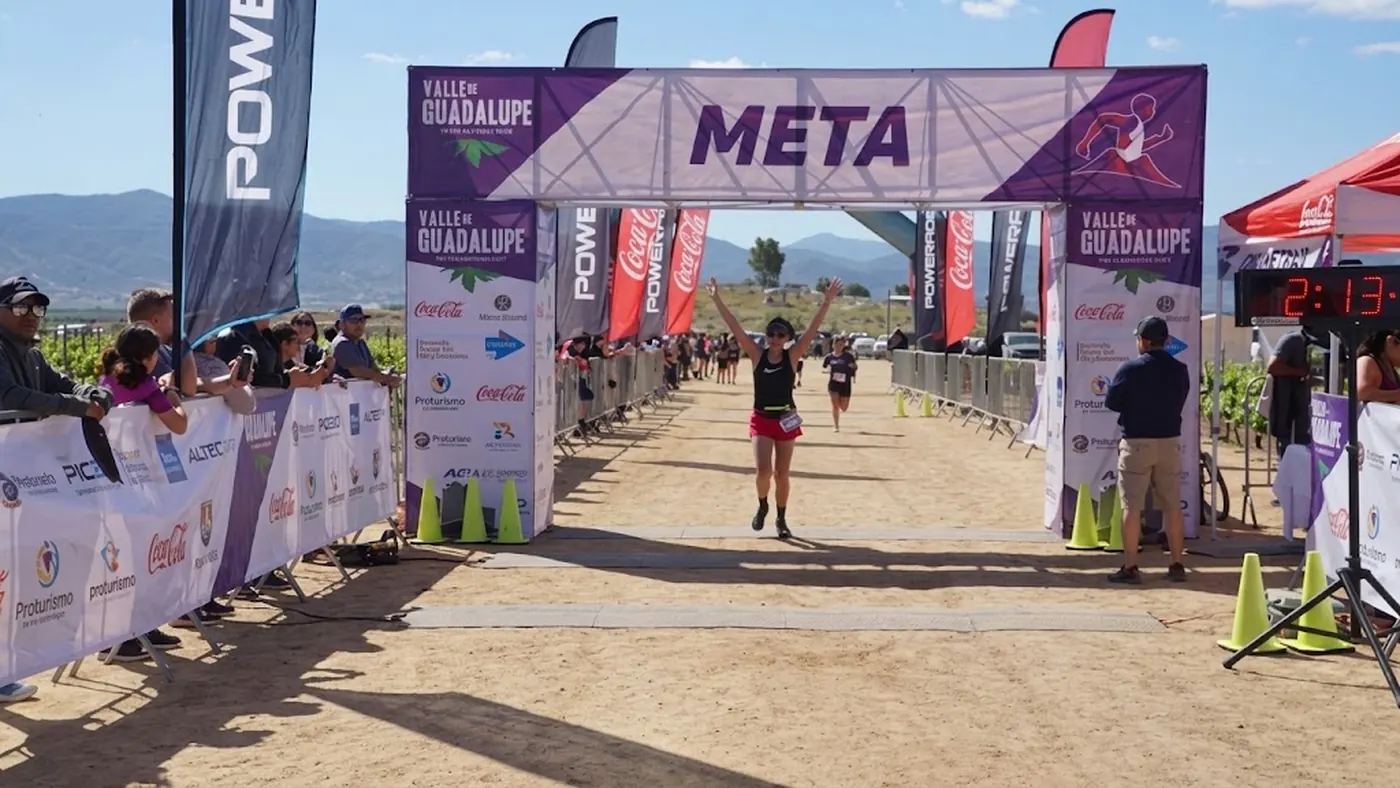 Corredora cruzando el arco de meta del medio maratón con la sierra del Valle de Guadalupe al fondo